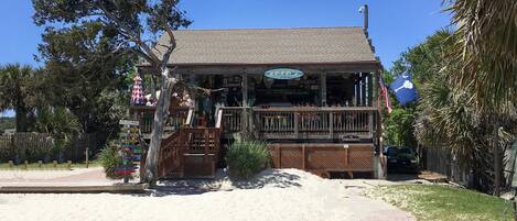A beachfront building with a signboard, a wooden deck, and a sandy area in front.