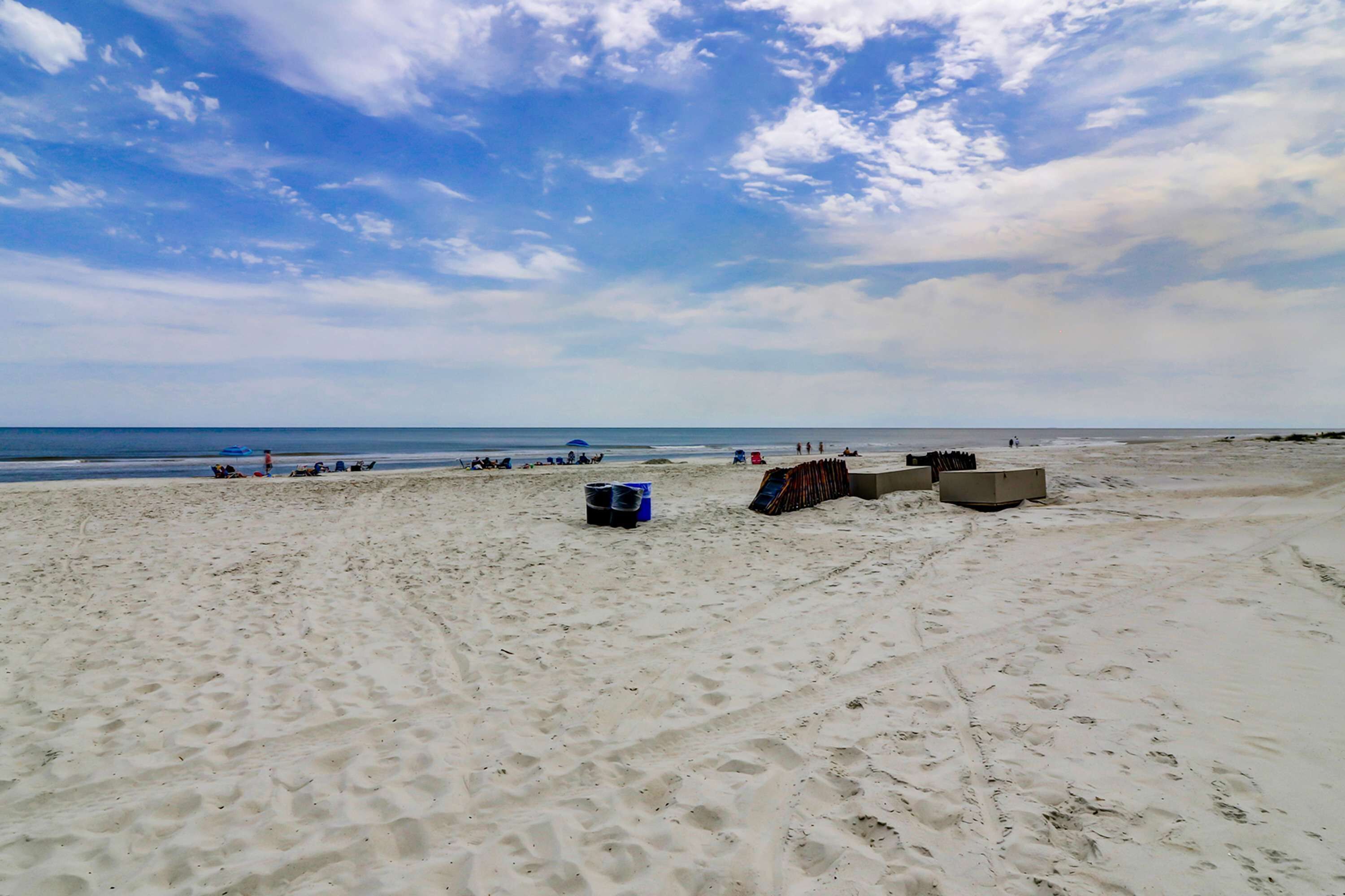 A sandy beach with footprints, a blue cooler, and a stack of chairs.