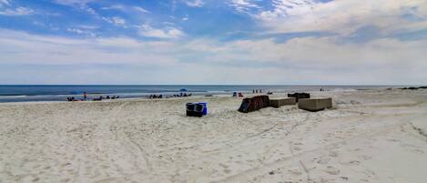 A sandy beach with footprints, a blue cooler, and a stack of chairs.