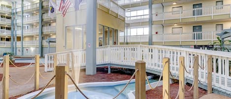 Un atrio interior de varios niveles con piscina, barandillas de madera y banderas.