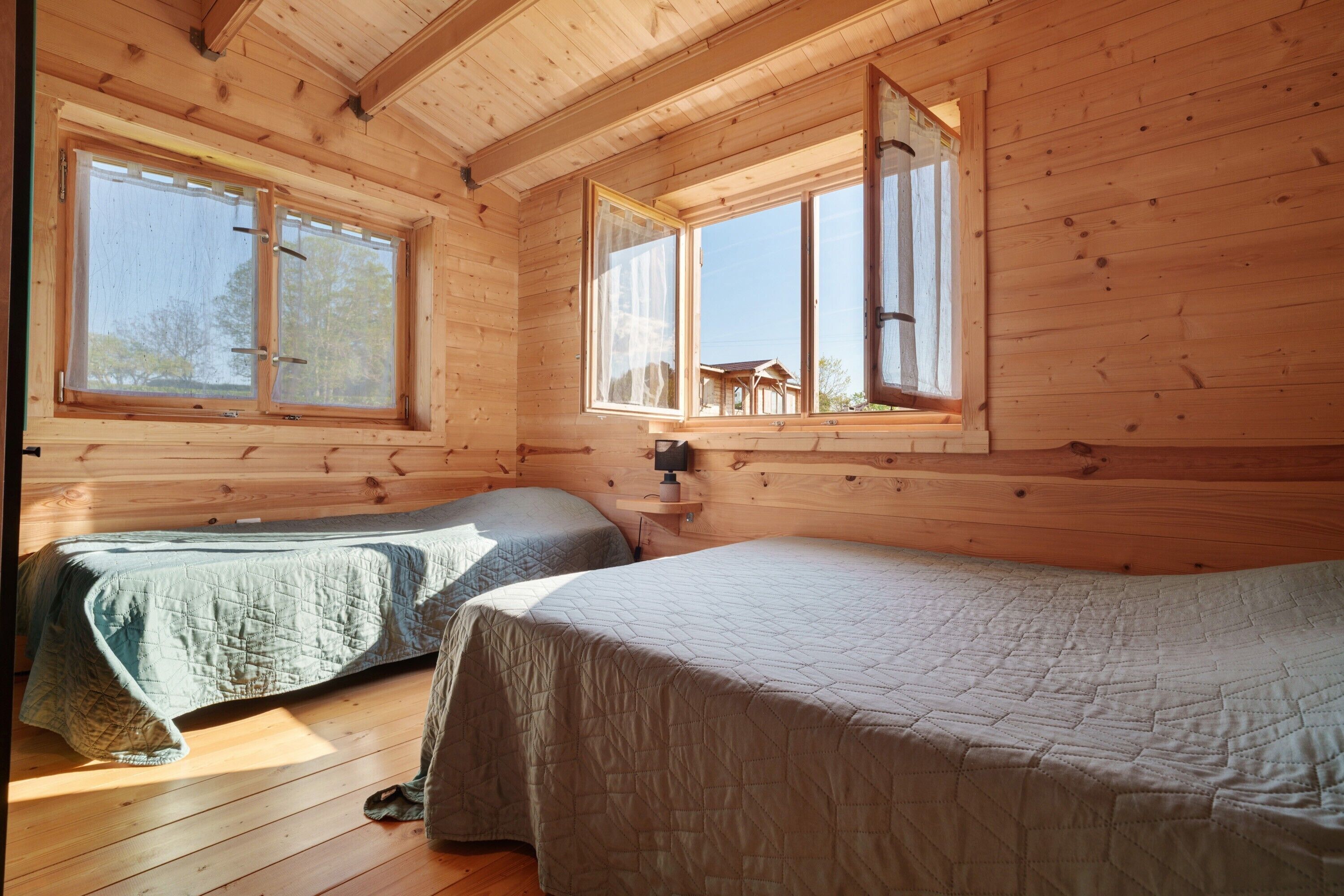 A cabin with two beds, wooden walls, and large windows.
