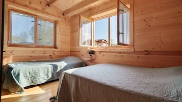 A cabin with two beds, wooden walls, and large windows.