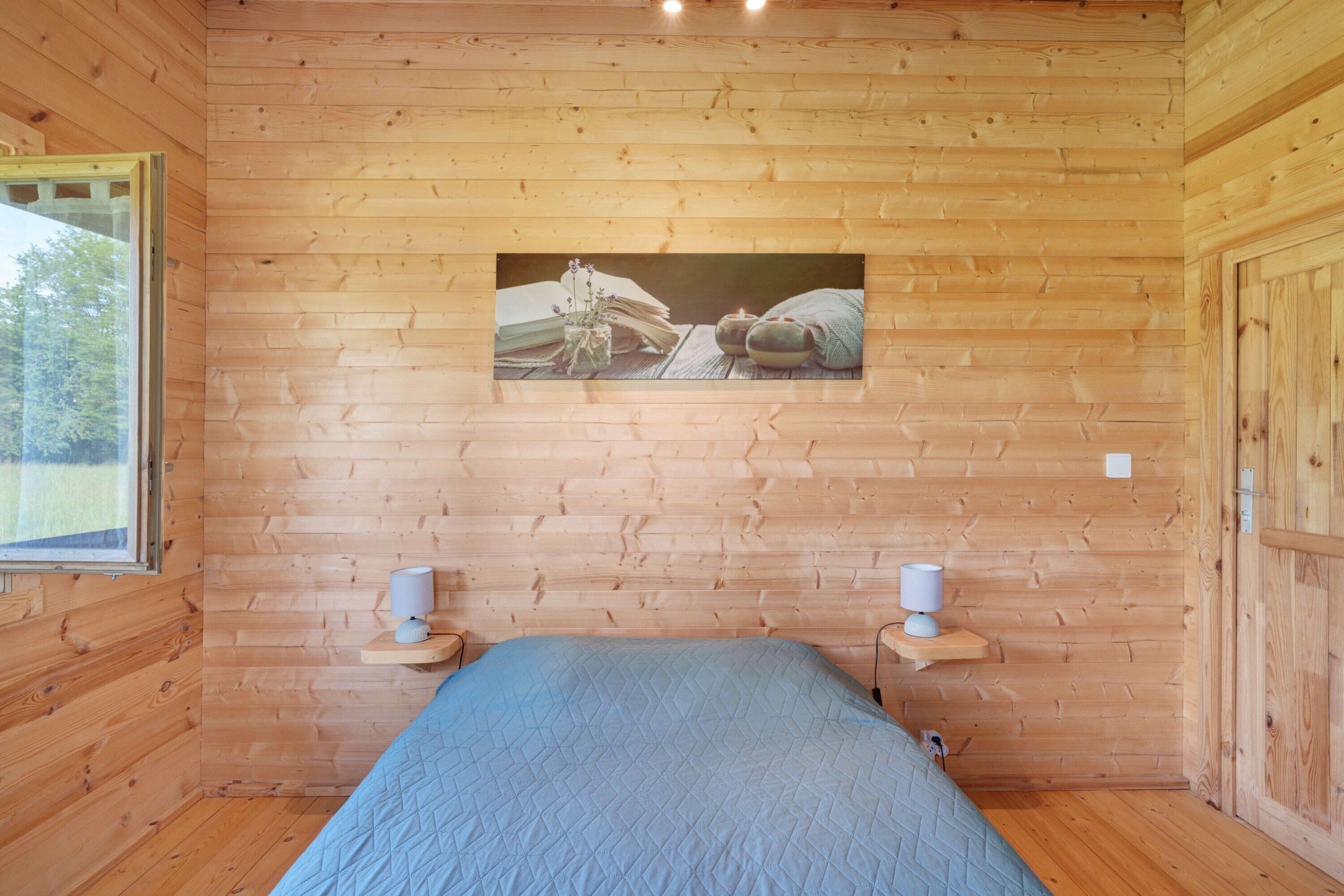 Quarto com painéis de madeira, uma cama, duas mesas de cabeceira, um quadro na parede e uma janela.