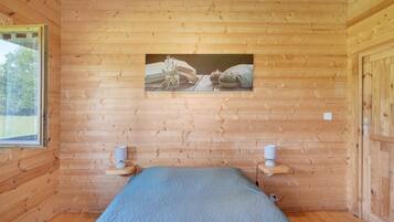 Quarto com painéis de madeira, uma cama, duas mesas de cabeceira, um quadro na parede e uma janela.