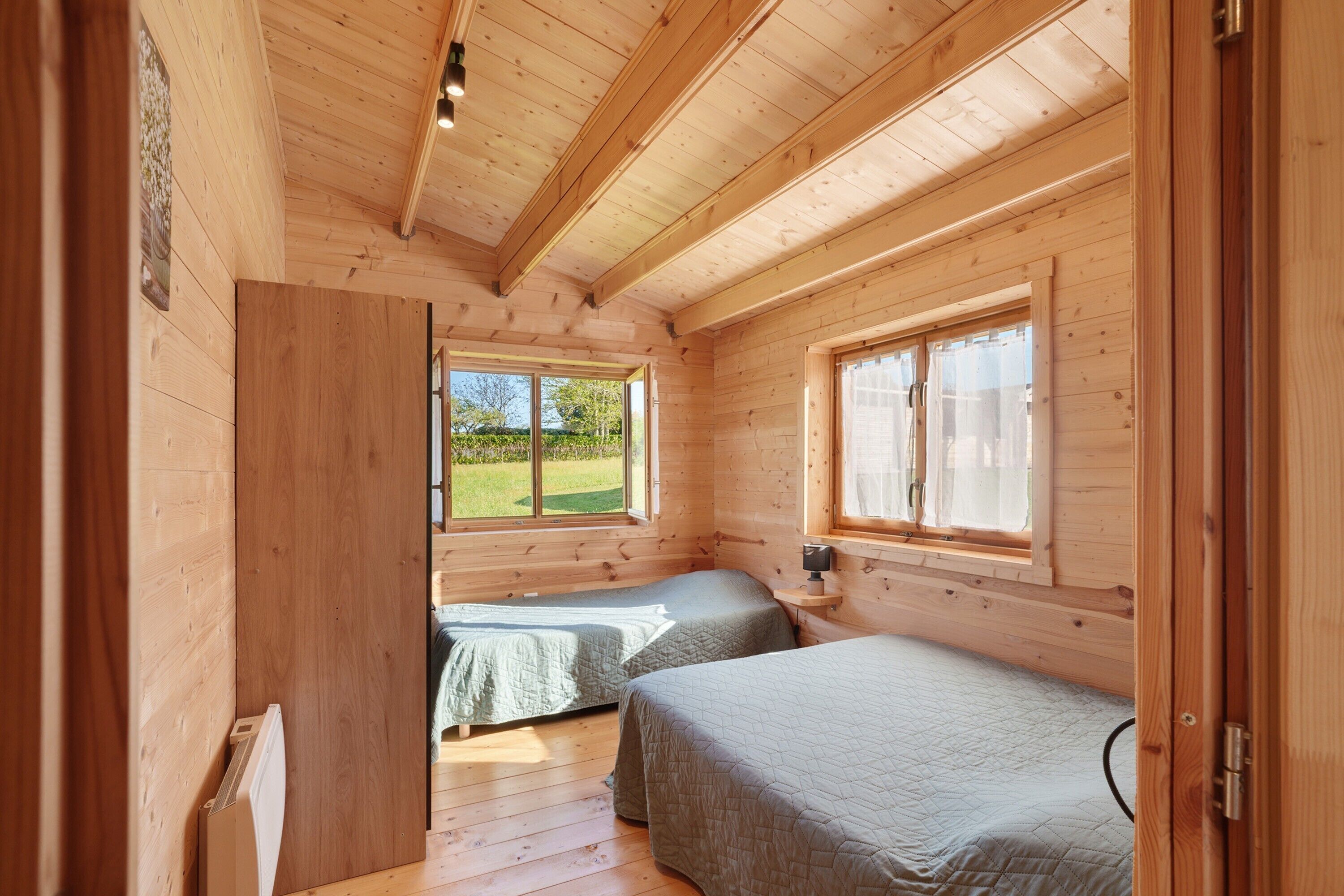 A wooden cabin room with two beds, a window, and a door.