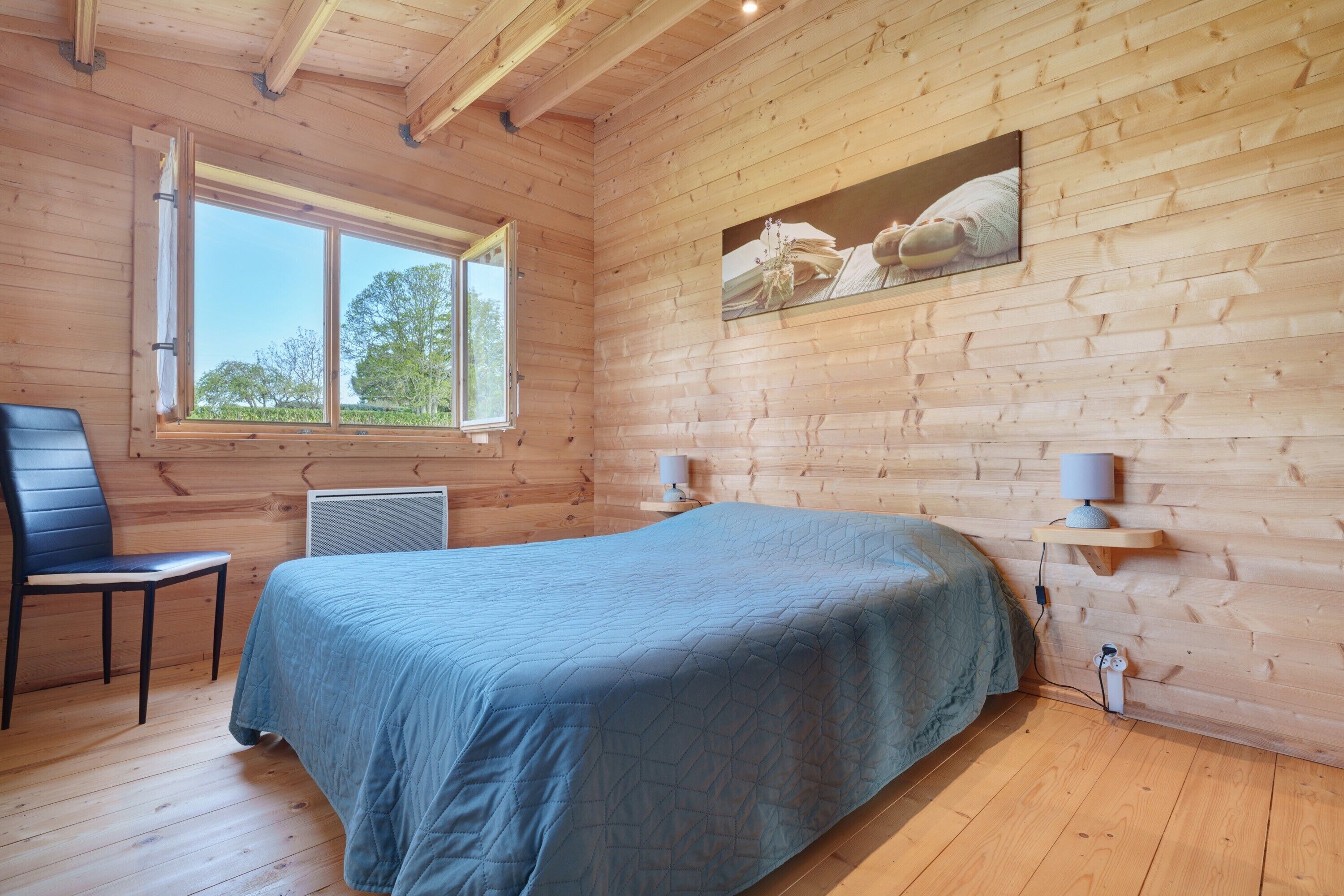 A wooden-paneled room with a bed, a chair, a window, and a wall-mounted lamp.