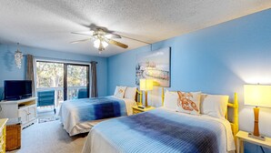 Quarto de hotel com duas camas, televisão, ventoinha no teto e uma janela grande.