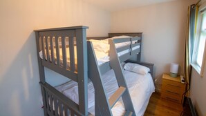 Une chambre avec un lit superposé, une table de chevet, une lampe et une fenêtre avec des rideaux.