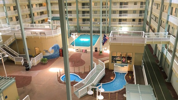 An indoor atrium with multiple balconies, a central swimming pool, and a children's play area. - Oceanside Resort Condo with Indoor Pool, Tennis & Oceanfront Restaurant (Hilton Head)