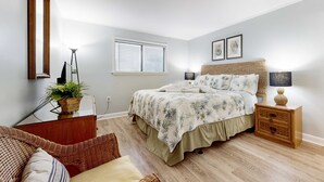 A bedroom with a bed, bedside tables, a lamp, a potted plant, a mirror, and a window with blinds. - Oceanside Resort Condo with Indoor Pool, Tennis & Oceanfront Restaurant (Hilton Head)