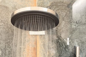 Ein moderner, runder Duschkopf mit mehreren Wasserstrahlen vor einer strukturierten Steinwand.