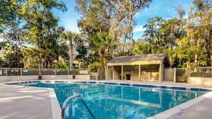 Piscina con área techada, rodeada de árboles y una valla.