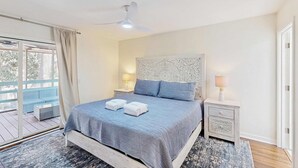 Un dormitorio con una cama, dos mesitas de noche, un ventilador de techo y vistas al exterior.