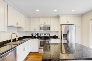 A modern kitchen with white cabinets, stainless steel appliances, and a granite countertop. - Coastal Comfort Near Shipyard Beach, Golf & Coligny (Hilton Head)