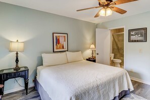 Una camera da letto con un letto, una ventola a soffitto, un comodino con lampada e un quadro appeso al muro.