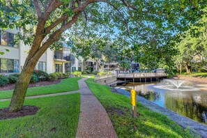 A pathway leading to a water feature with a bridge, surrounded by greenery and modern buildings. - Well appointed home with path to the beach, pool, private washer, dryer & AC (Hilton Head)