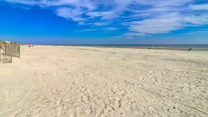 En sandstrand med ett trästaket till vänster och en klarblå himmel.
