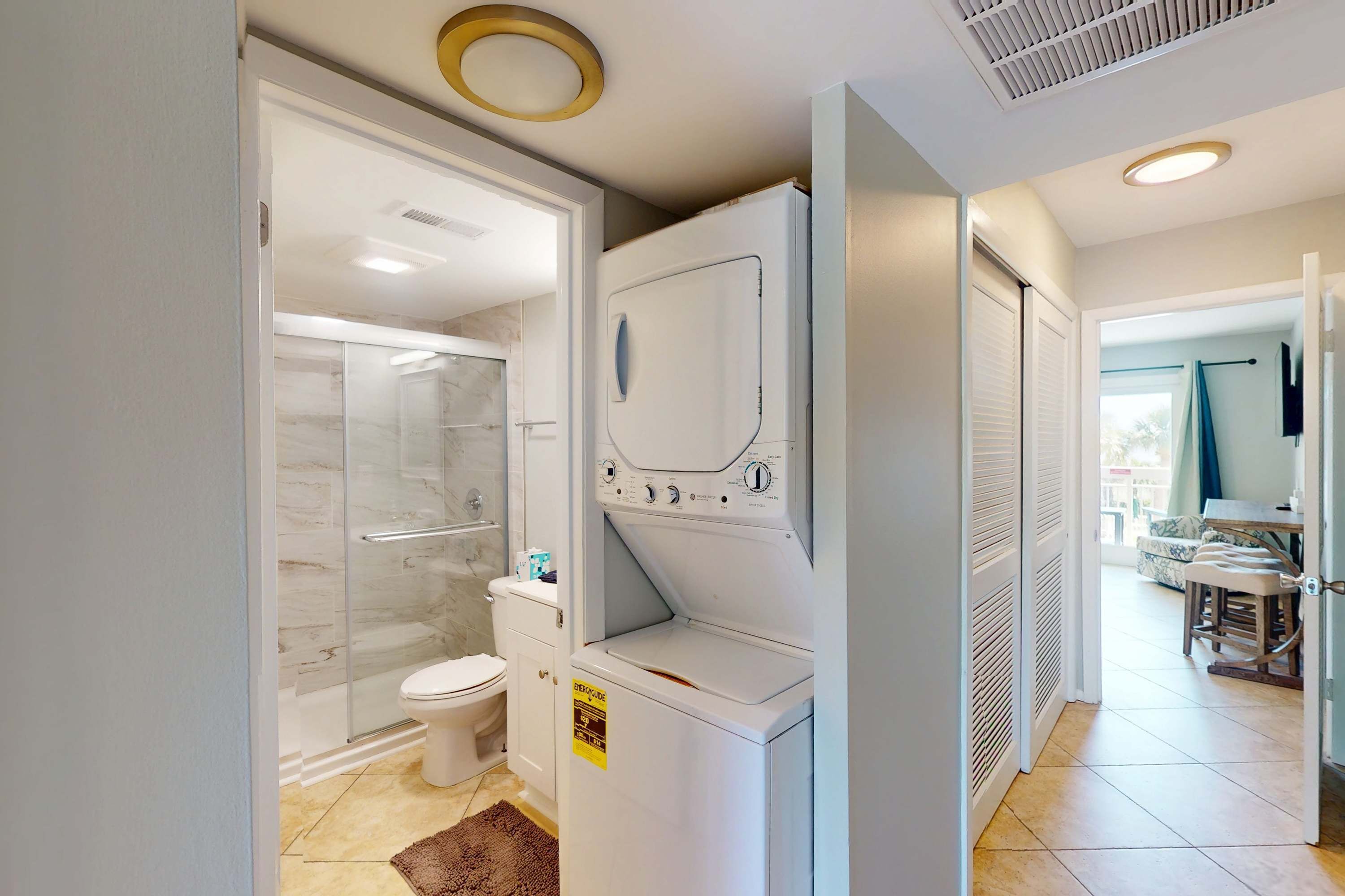 A compact bathroom with a glass shower enclosure, a toilet, and a stacked washer and dryer unit.