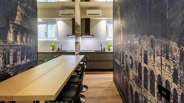 A modern kitchen with a long table and chairs, air conditioning units, and a view of the cityscape through large windows. - Emotional Shower & Absolute Silence (Rome)