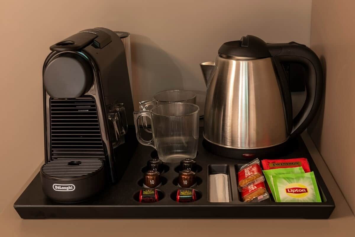 Une machine à café, une bouilloire, une tasse en verre et quelques sachets de thé Lipton, le tout disposé sur un plateau.