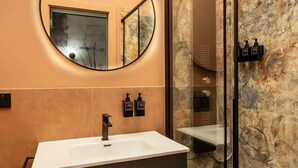 A modern bathroom with a large oval mirror, a white sink, and a glass-enclosed shower. - Emotional Shower & Absolute Silence (Rome)