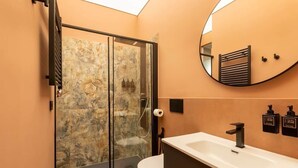 Un baño moderno con cabina de ducha de vidrio, un lavamanos blanco y un espejo.