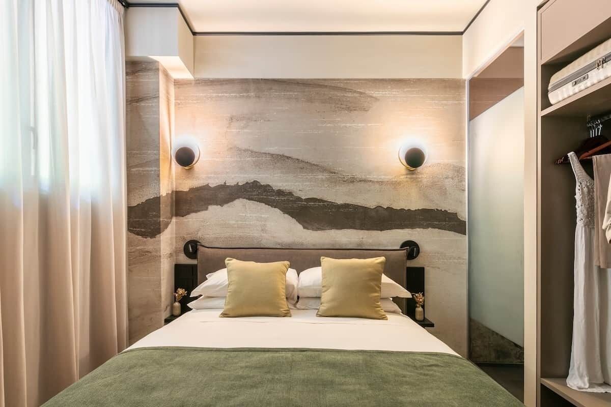 Ein Hotelzimmer mit einem Bett, zwei Wandleuchten, einem Kopfteil und einem Kleiderschrank mit Kleidung.