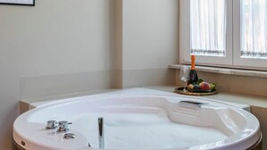 Ein modernes Badezimmer mit freistehender Badewanne, einem gerahmten Kunstwerk an der Wand und einem Fenster mit transparenten Vorhängen.
