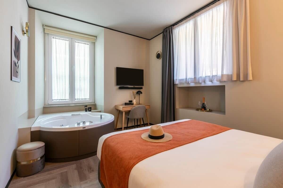 Ein Hotelzimmer mit Bett, Schreibtisch, Fernseher, Badewanne und einem Fenster mit Vorhängen.