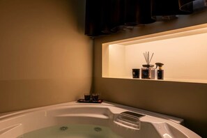 Ein modernes Badezimmer mit einer großzügigen Badewanne, einem Ablagefach für Pflegeprodukte und einem an der Wand montierten Fernseher.