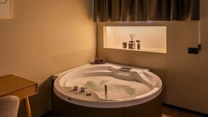 A modern bathroom with a freestanding bathtub, a small table, and a shelf with toiletries. - Relax Hot Tub – San Giovanni (Rome)