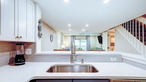 A kitchen with a stainless steel sink, white cabinets, a blender, and a staircase leading to another level.