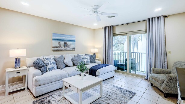 A living room with a sofa, a coffee table, a painting, and a balcony with curtains.