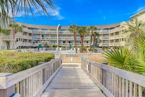A multi-story hotel with balconies, a pool area, and a wooden boardwalk leading to the entrance. - Beach-view condo in oceanfront complex with outdoor pool, beach access & balcony (Hilton Head)