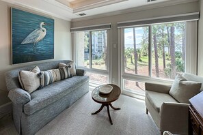 Un salon avec un canapé gris, une table ronde et un tableau représentant un oiseau.