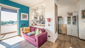 A living room with a sofa, a kitchen area, a white brick wall, and a view through a window. - Il Favoloso Mondo di Vale (Marino)