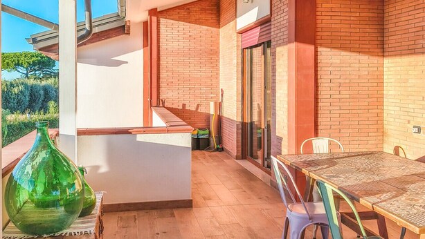 A covered patio area with a wooden table and chairs, a green vase, and a brick wall. - Il Favoloso Mondo di Vale (Marino)