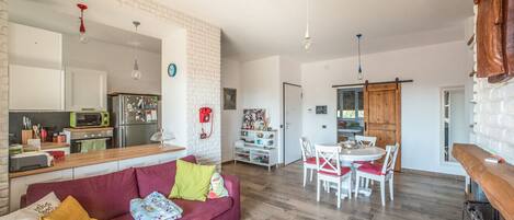 A modern living space with a red sofa, wooden flooring, a kitchen with a microwave, and a dining area with white chairs.