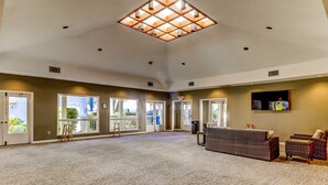 A spacious room with a high ceiling, large windows, and a seating area with wicker furniture. - End unit, 3rd floor Apartment near beach with balcony, pool, & tennis (Hilton Head)