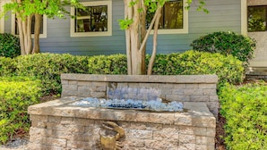 A stone fountain with water spouting from the center, surrounded by well-maintained hedges and trees. - End unit, 3rd floor Apartment near beach with balcony, pool, & tennis (Hilton Head)