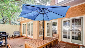 Un patio al aire libre con mesa y bancos de madera, una sombrilla azul y una parrilla.
