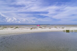 Ein Strand mit einem pinken Sonnenschirm, ruhigem Wasser und weiter Küste.