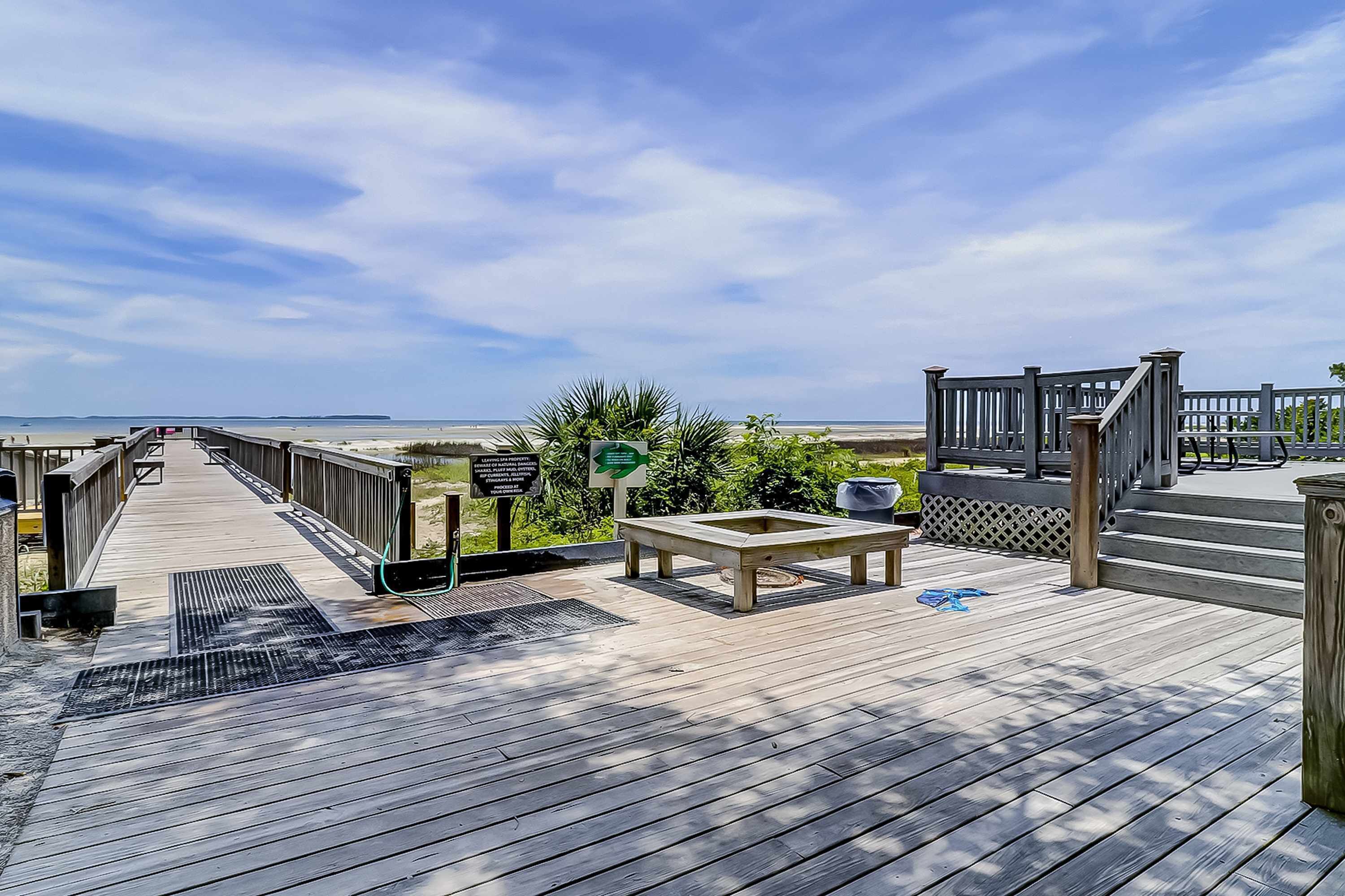 A wooden deck with a view of the beach, a picnic table, and a covered area with steps.