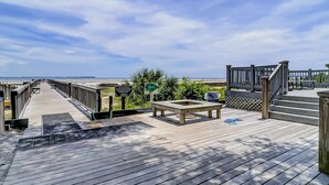 A wooden deck with a view of the beach, a picnic table, and a covered area with steps. - Vibrant condo with tennis courts, pool, WD, gas grill, balcony, & playground (Hilton Head)
