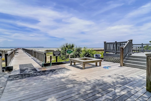 A wooden deck with a view of the beach, a picnic table, and a covered area with steps. - Vibrant condo with tennis courts, pool, WD, gas grill, balcony, & playground (Hilton Head)
