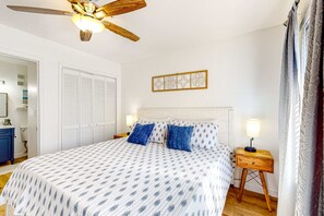 Ein Schlafzimmer mit Bett, Deckenventilator, Nachttisch mit Lampe sowie Wandkunst.