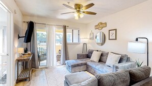 A living room with a sectional sofa, a ceiling fan, a small table with a lamp, and a sign that reads 'Beach House'. - Vibrant condo with tennis courts, pool, WD, gas grill, balcony, & playground (Hilton Head)
