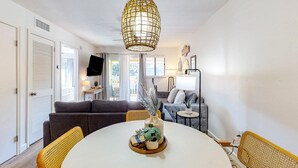 A modern living room with a round dining table, a sofa, and a television. - Vibrant condo with tennis courts, pool, WD, gas grill, balcony, & playground (Hilton Head)
