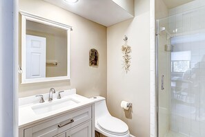 A bathroom with a white sink, mirror, toilet, and glass shower enclosure. - Fun & bright beach getaway with pool, easy beach access & pond view (Hilton Head)