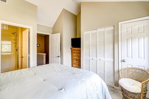 A bedroom with a bed, a dresser, a television, and a wicker chair. - Fun & bright beach getaway with pool, easy beach access & pond view (Hilton Head)